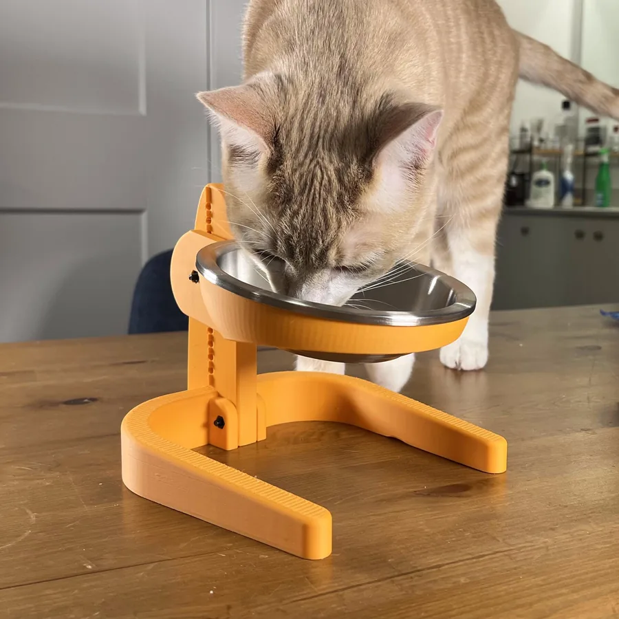 Künefe, a ginger tabby, eating from a stainless steel bowl held at head height by an orange 3D-printed stand