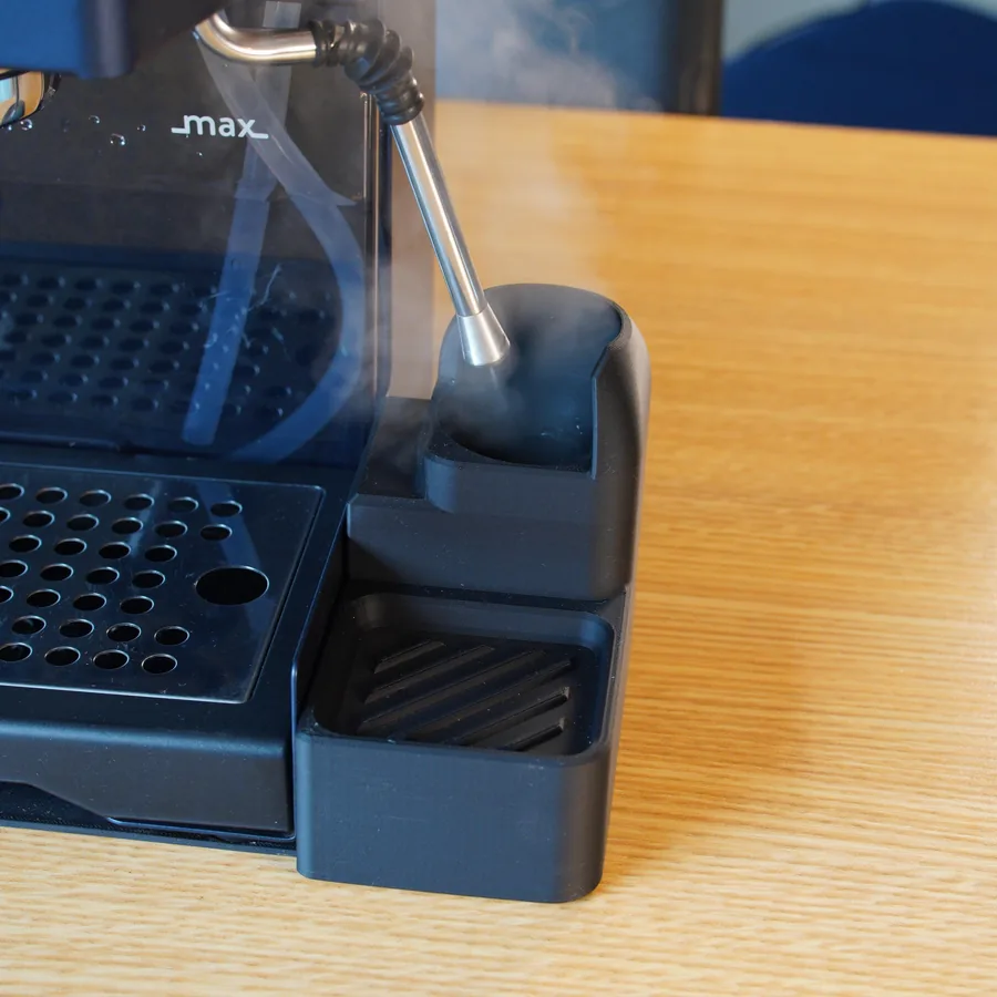 A black 3D-printed tray clipped to the side of a Gaggia Classic, with the steam wand purging into it